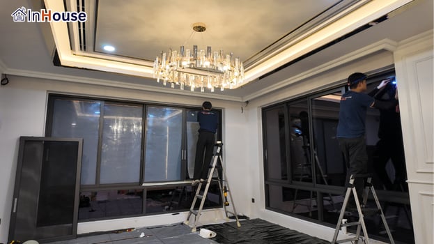 Installing the dining-room glass smart film The crew finishes under the crystal chandelier — Khun Kang — Smart Film for the Dining and Living Rooms, Korat